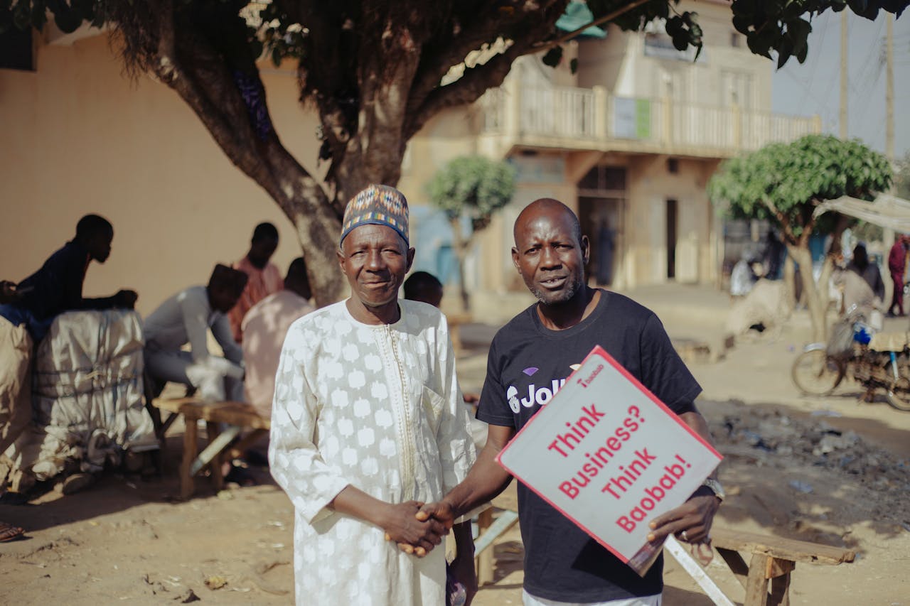 services-02 Two African men shaking hands outdoors with a business sign, community setting.