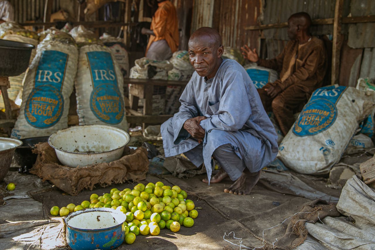 gallery-3 A man at a local market in Maiduguri, Nigeria surrounded by bags of flour and fresh produce.