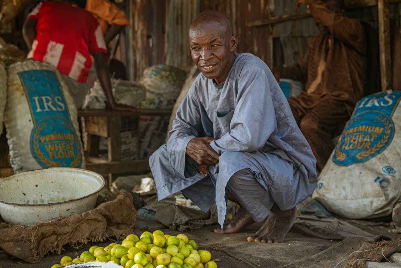 why-choose-us Portrait of a man squatting in a bustling African market in Maiduguri, Nigeria.